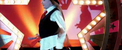 A gif from the film Little Miss Sunshine. A girl on a stage throws her top hat gleefully aside, ready to dance.