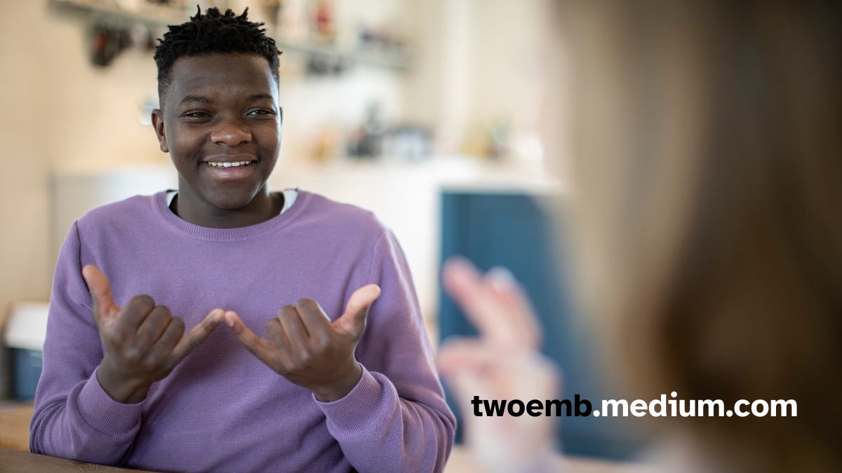 image of a Black man in purple sweater signing “now” in American Sign Language