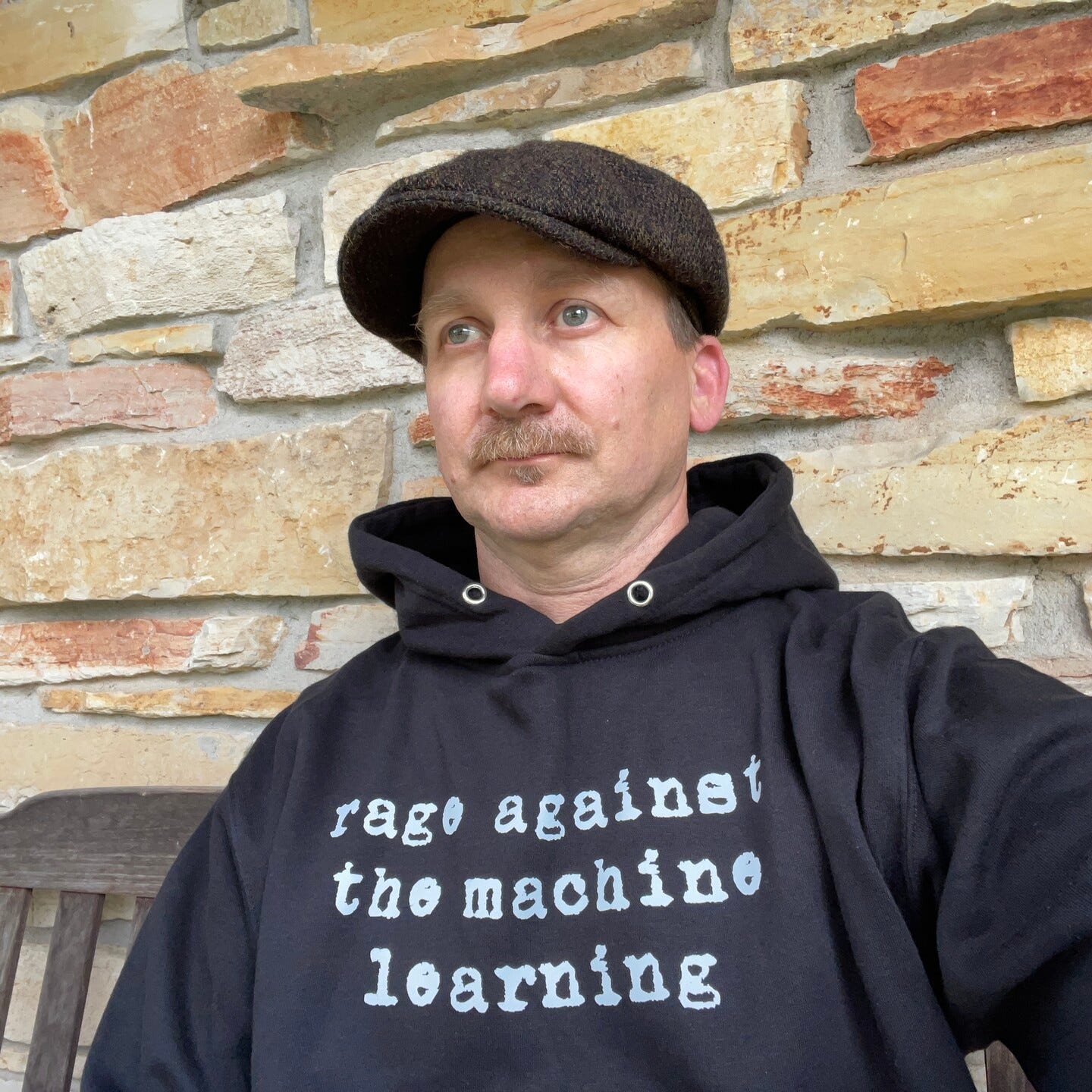 @kbroman in black hoodie that reads “rage against the machine learning” in white letters in a typewriter font. He’s also wearing a tweed newsboy hat and is trying to emulate a model by staring into the distance.