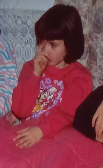 A photo of me as a young child sucking my thumb. I'm wearing a bright pink minnie mouse dress and am covered in a bright pink blanket