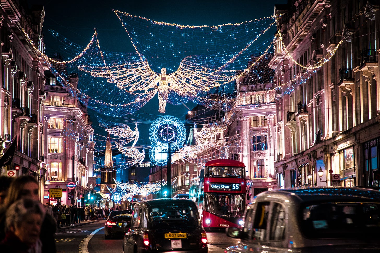 Blue and white lights over Oxford Street, an angel decorated above the street, double decker bus and other traffic below