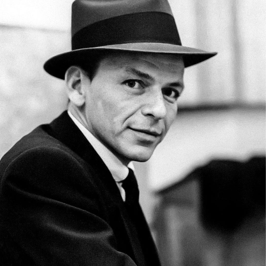A black and white image of Frank in his prime. He is looking quite dapper in a suit and hat, and as turned to face the camera. His eyes pierce the shot.