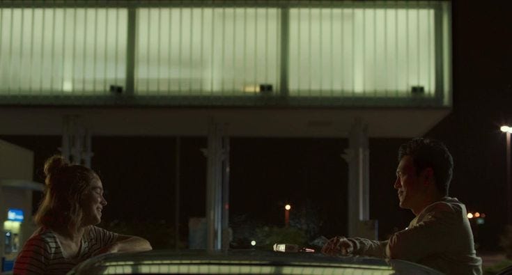 This may contain: a man and woman sitting on a bench in front of a tall building at night