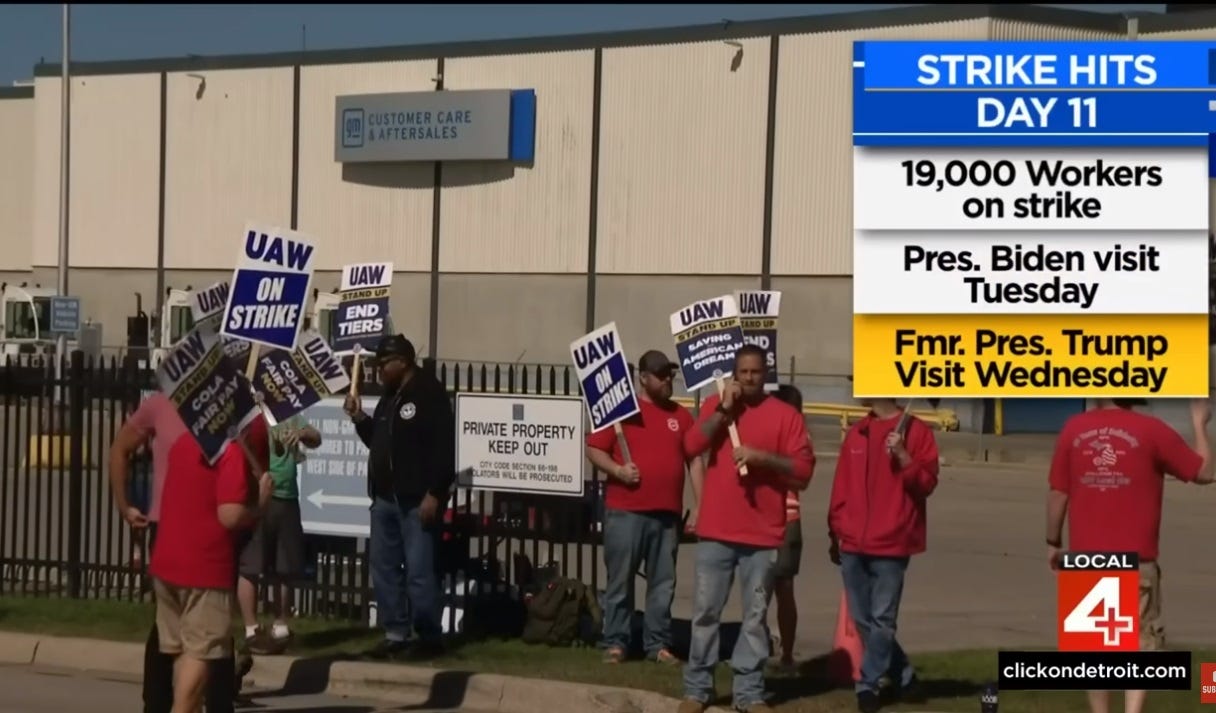 Video screenshot showing UAW members in red T-shirts striking outside a General Motors parts warehouse; they carry signs reading 'UAW On Strike,' 'Stand Up: Saving the American Dream,' 'End Tiers,' and 'COLA/Fair Pay Now.'  TV station graphic reads 'Strike hits day 11;  19,000 workers on strike; Pres. Biden visit Tuesday; ' Fmr. Pres. Trump Visit Wednesday'