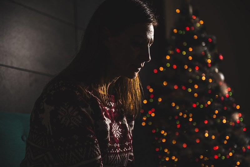 This shows a depressed looking woman sitting by a christmas tree