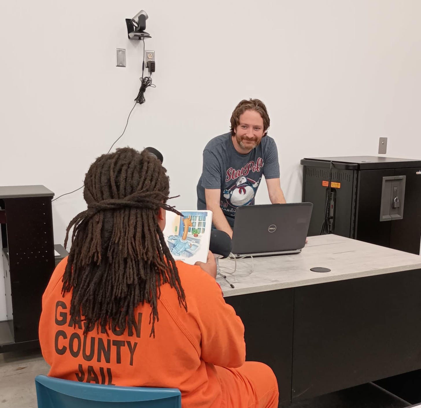 A resident at the Gaston County Jail reads a children's picture book. Dondero is at a laptop, recording the individual's voice as they read. 