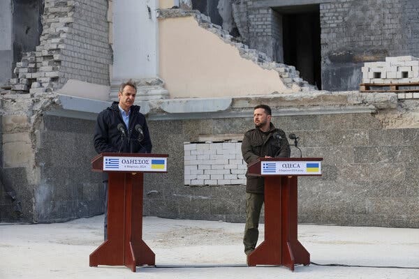 Two men standing behind lecterns near the foundations of a building.