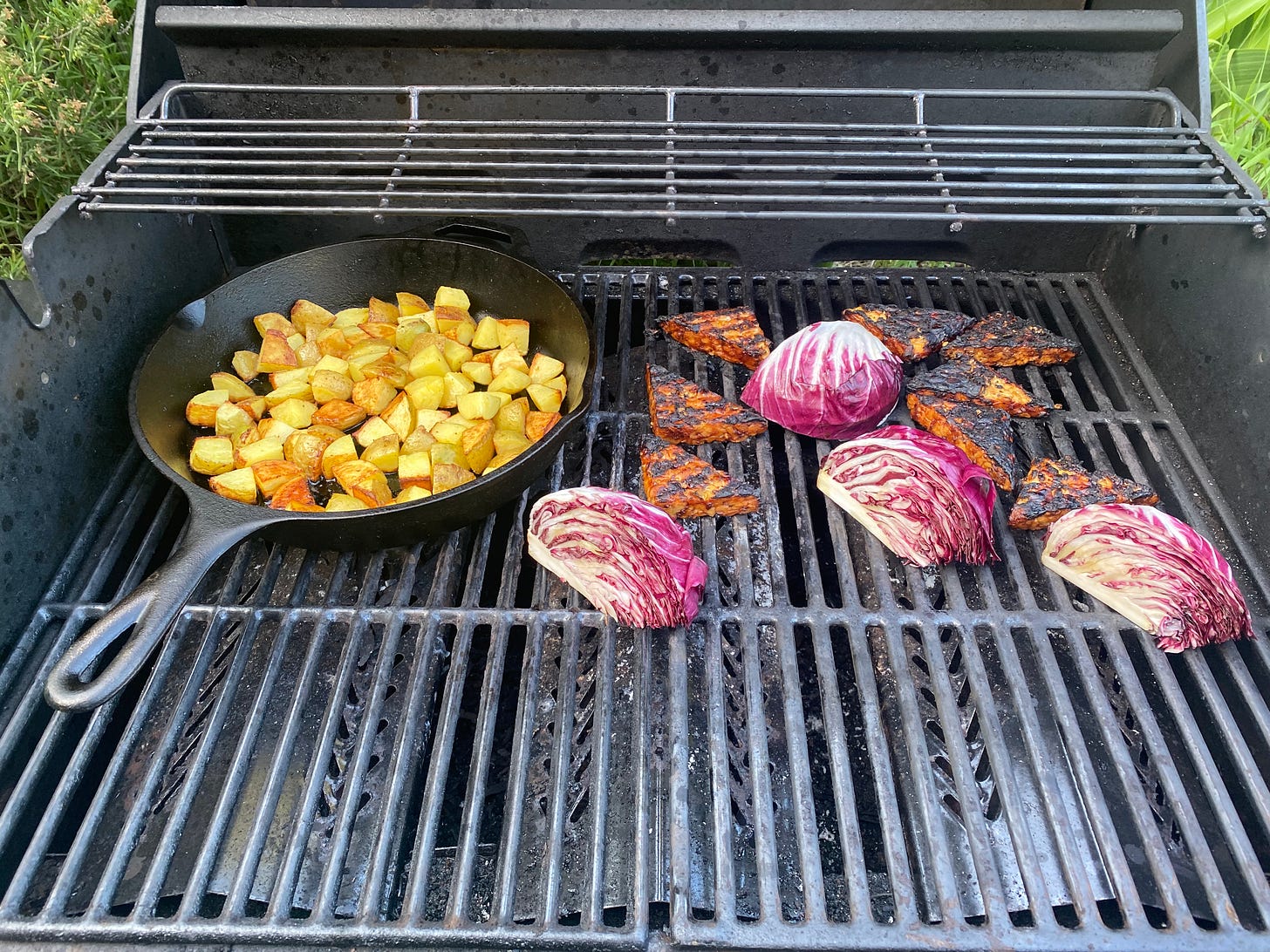 Various things on the grill: a cast iron pan of diced potatoes, triangles of blackened tempeh, and wedges of radicchio.