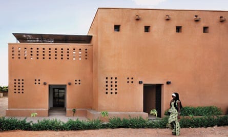 A woman walks past a building made with unfired earth bricks