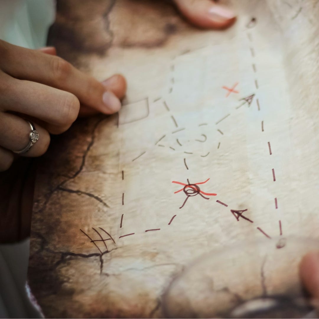 A paper map with hand drawn paths and locations with question marks on it. Two pairs of hands examine the map together.
