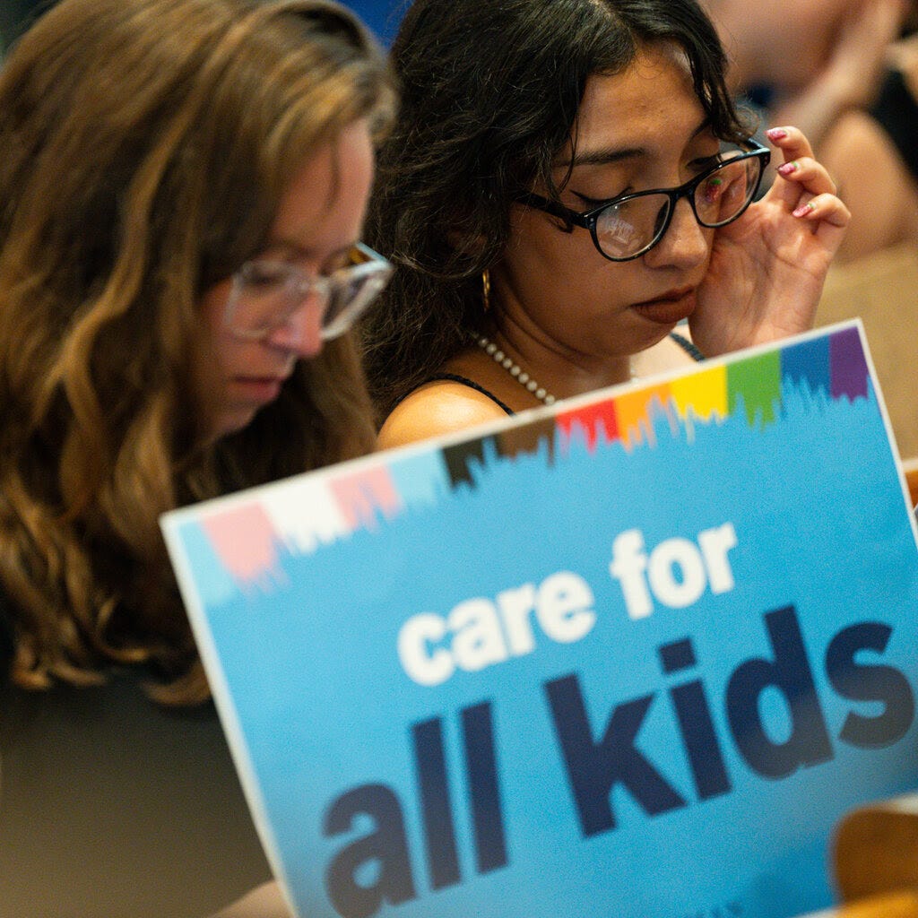 Two people near a sign that says “Care for All Kids.”