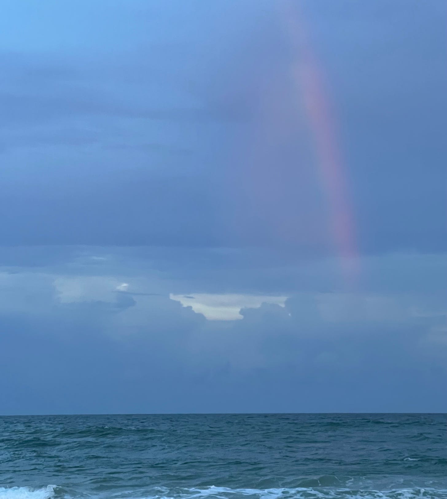 a rainbow appears in a blue twilight, cloudy sky over the ocean