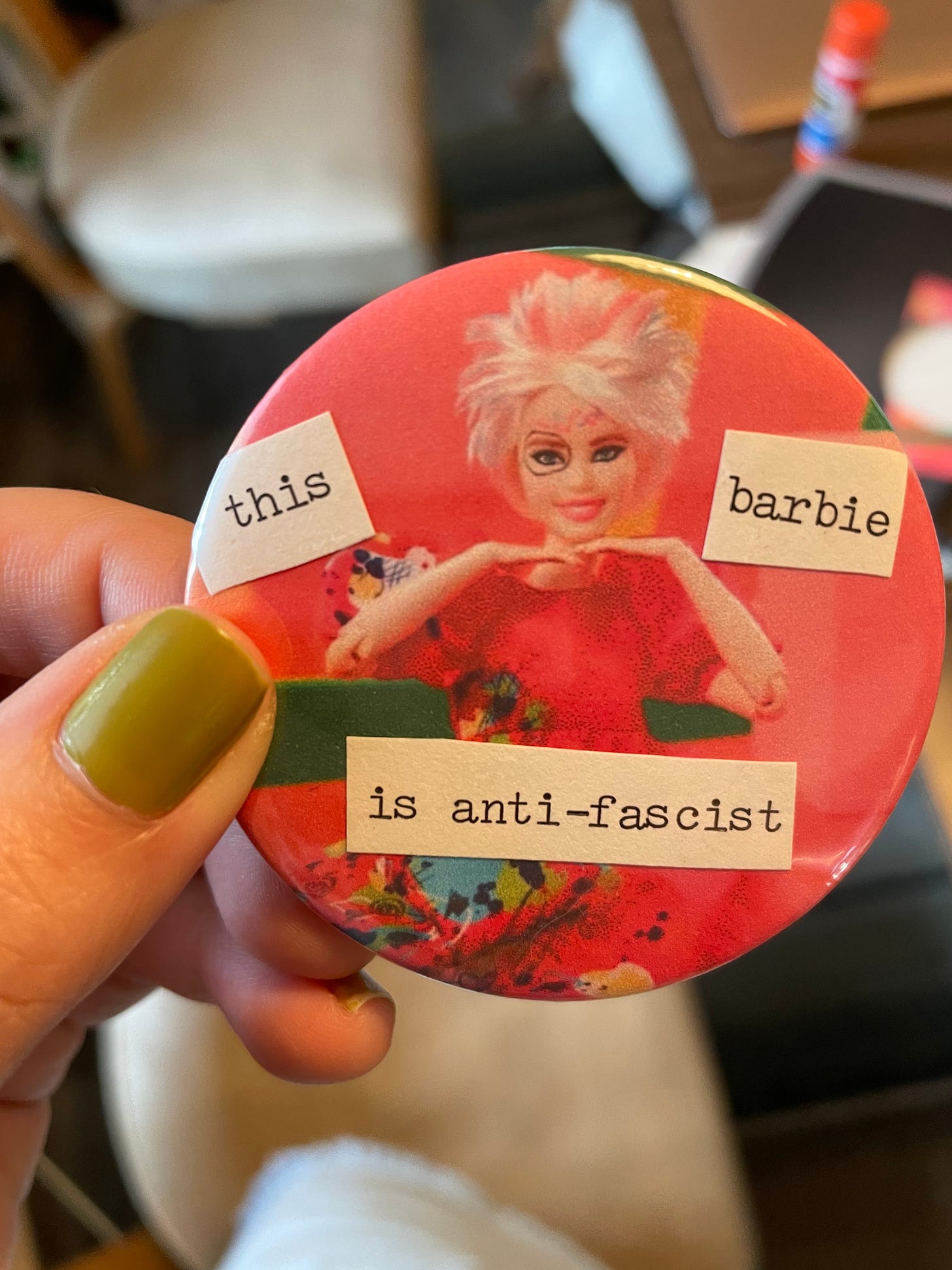 a pink button of weird barbie from the barbie movie--a barbie with its hair cut short and with marker drawings on her face. black type on white background is cut up and says this barbie is anti-fascist