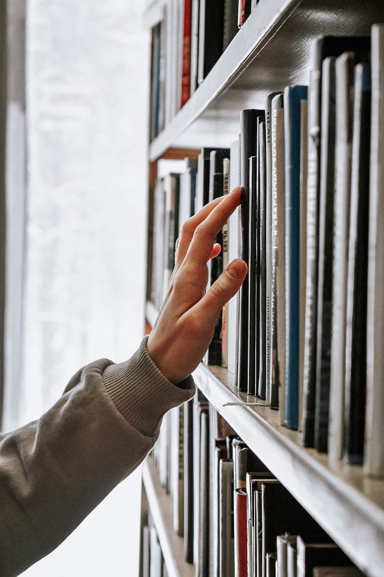 Person touching a book on a library shelf