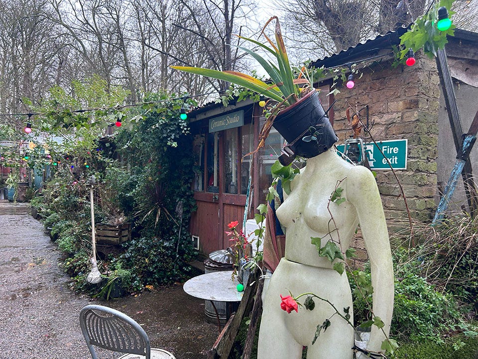 A mannequin stands in front of a shed covered with greenery on Eel Pie Island.