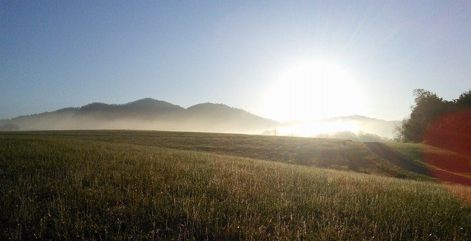 A sunrise scene with mountains in the background, and a grassy field in the foreground.