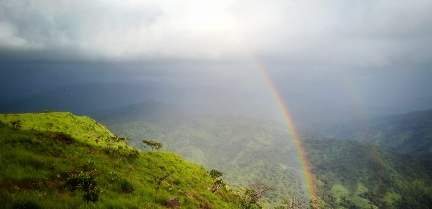 A green hill beneath clouds with a rainbow arcing from below.
