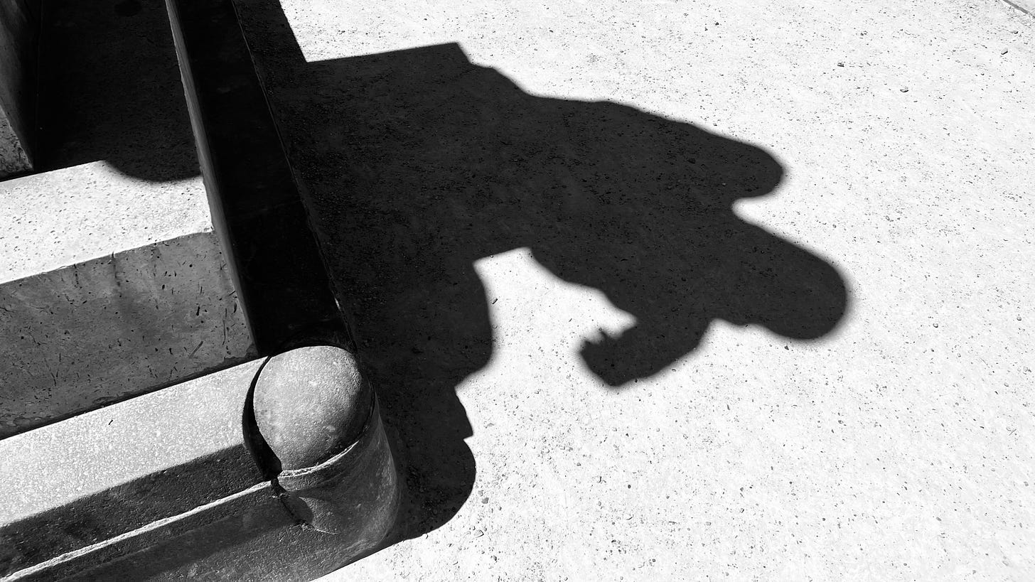 Photo of a corner of a statue's pedestal and the statue’s shadow on a bright background.