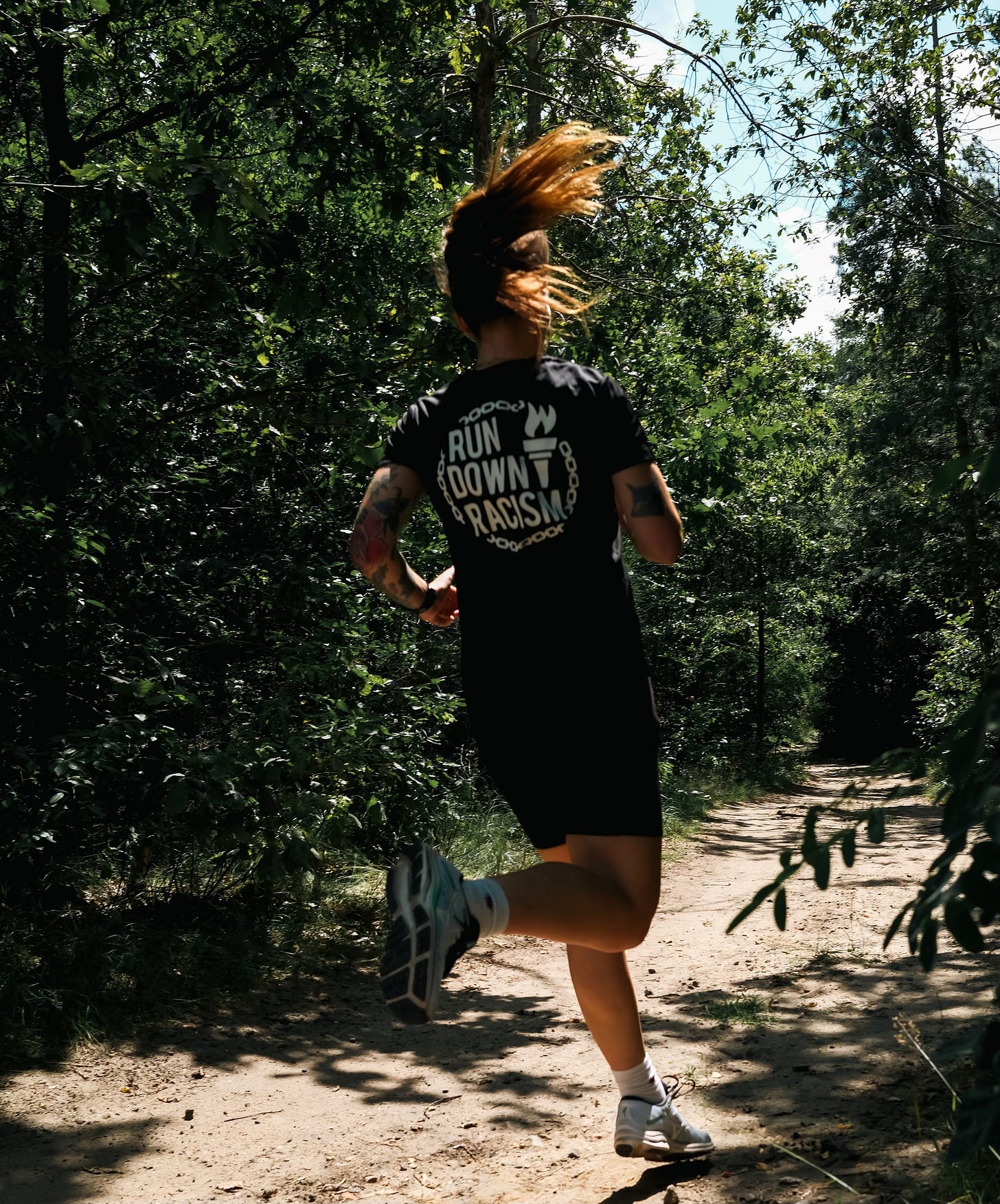 Female runner wearing a "Run Down Racism" shirt running through the woods