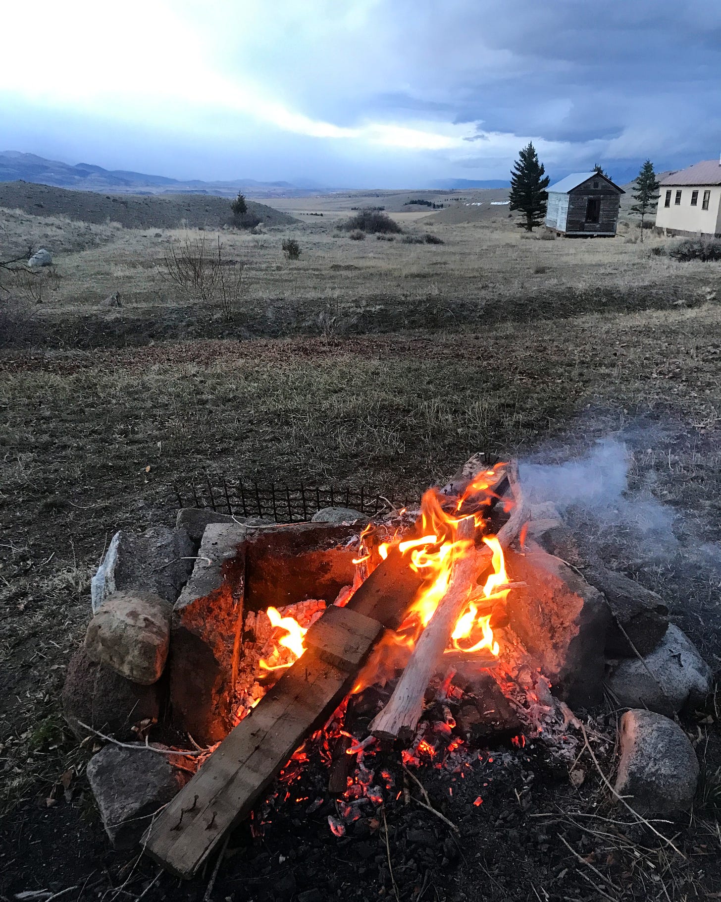 Campfire with small buildings on right, long view up cloudy Paradise Valley