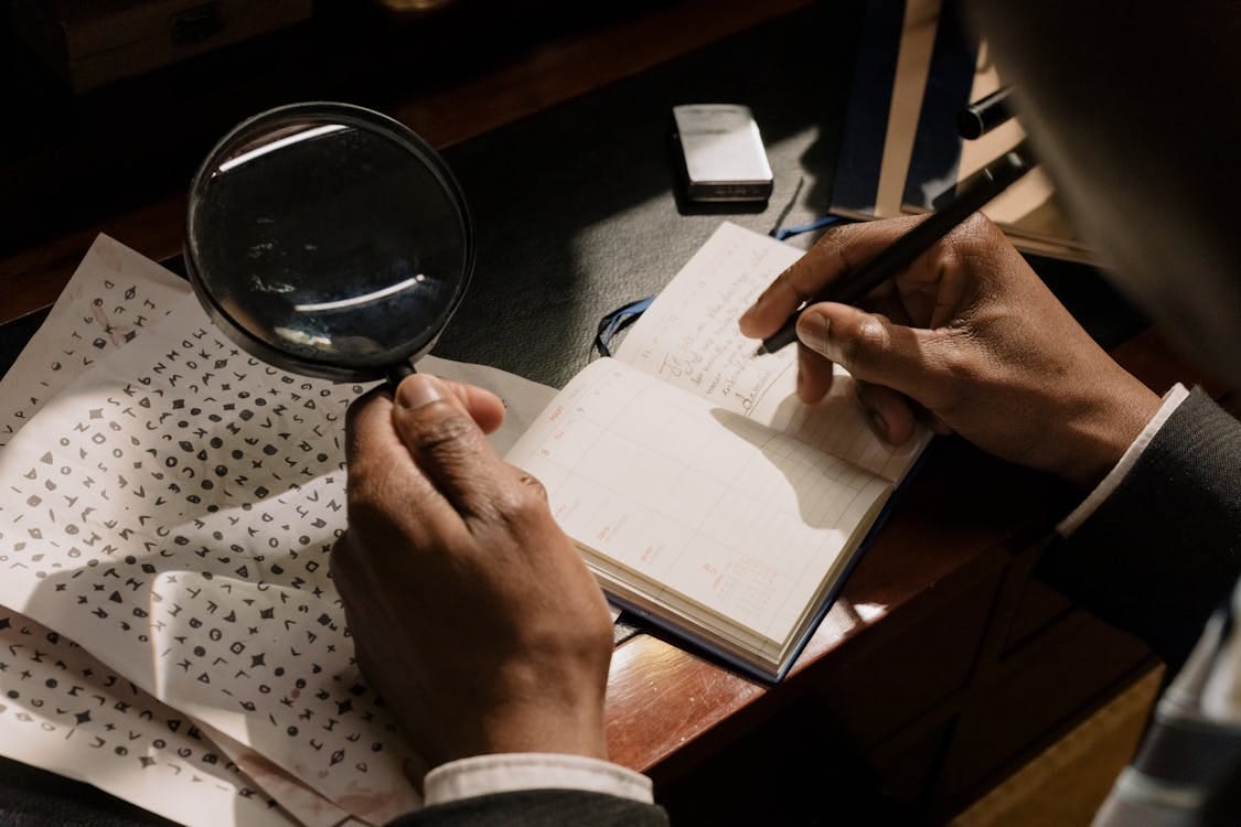 Free A detective decoding cipher documents with a magnifying glass, notebook in hand. Stock Photo