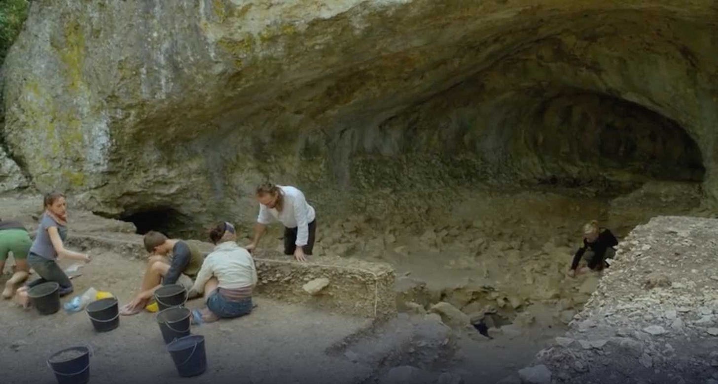 An archaeological dig at the edge of a cave with workers present
