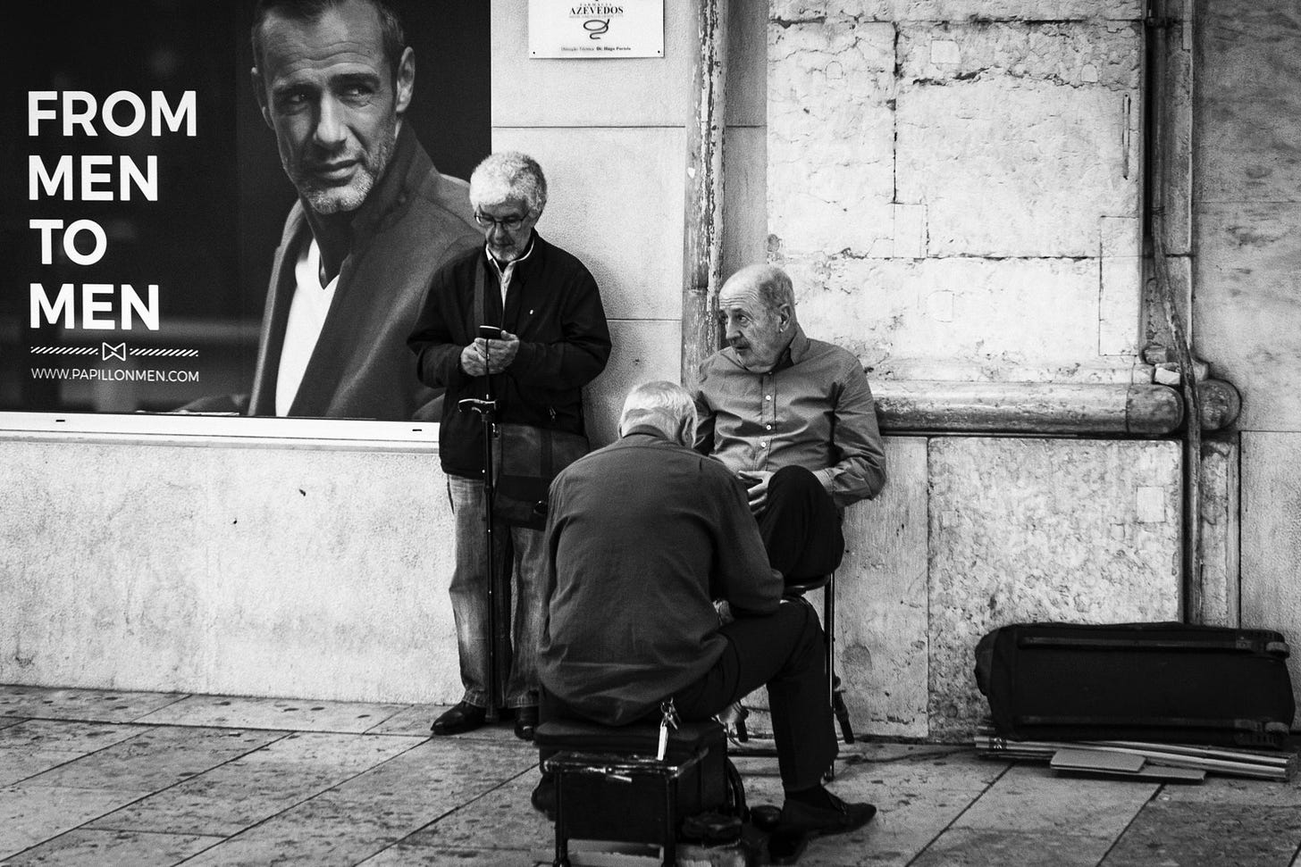 three men in the street are seen in front of an ad that states "from men to men"