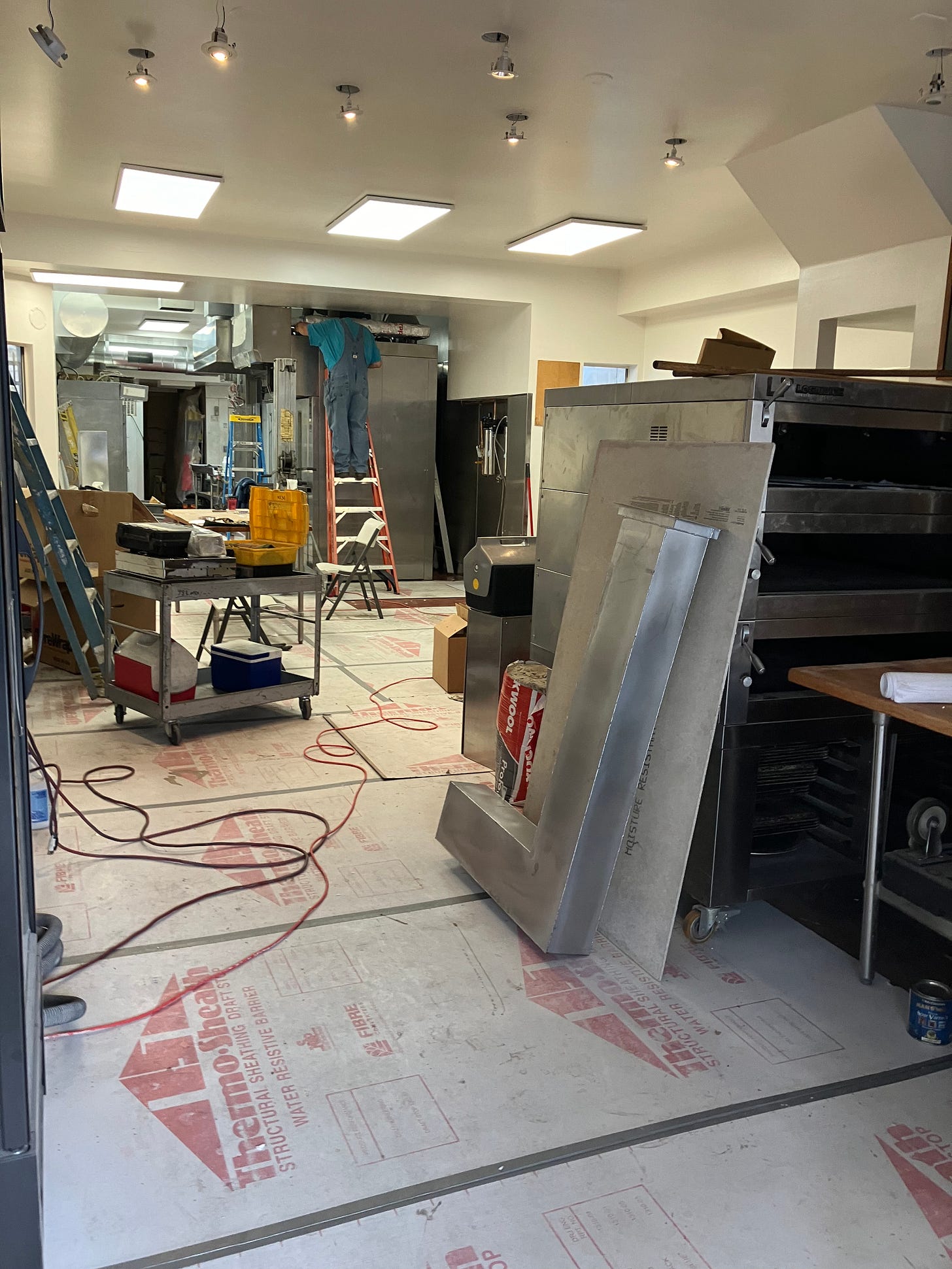 a pictuer of the inside of a bakery that has been taken apart to install a new oven. lots of construction equipment and materials inside a bakery