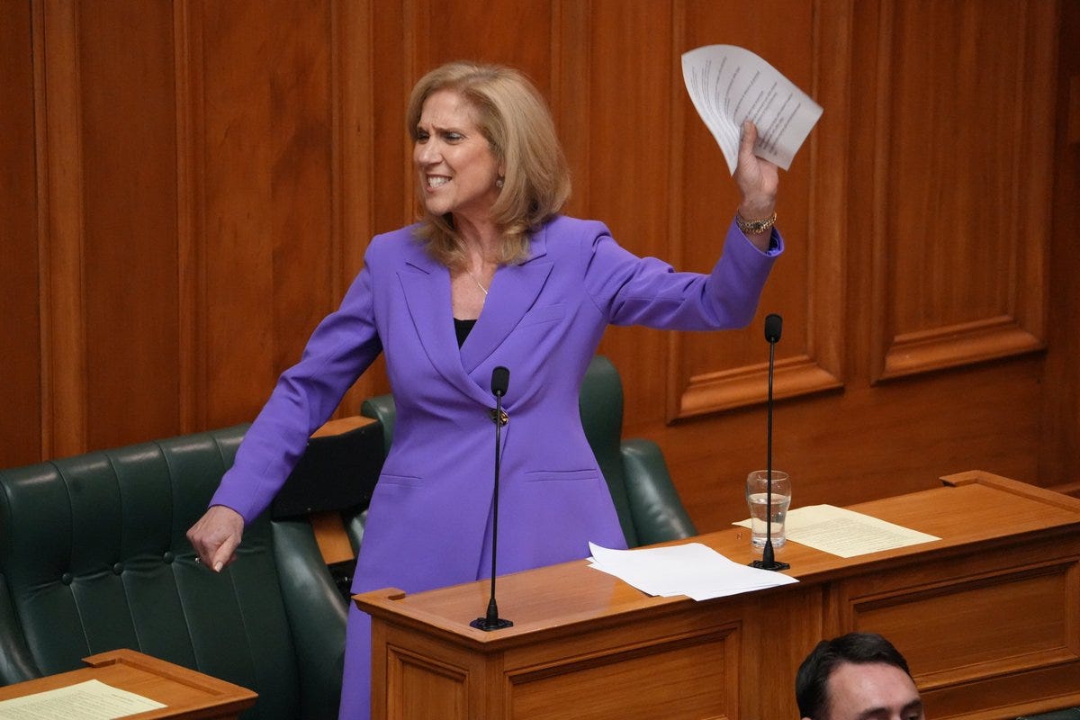 a blonde woman in a purple dress holds up a document in parliament house