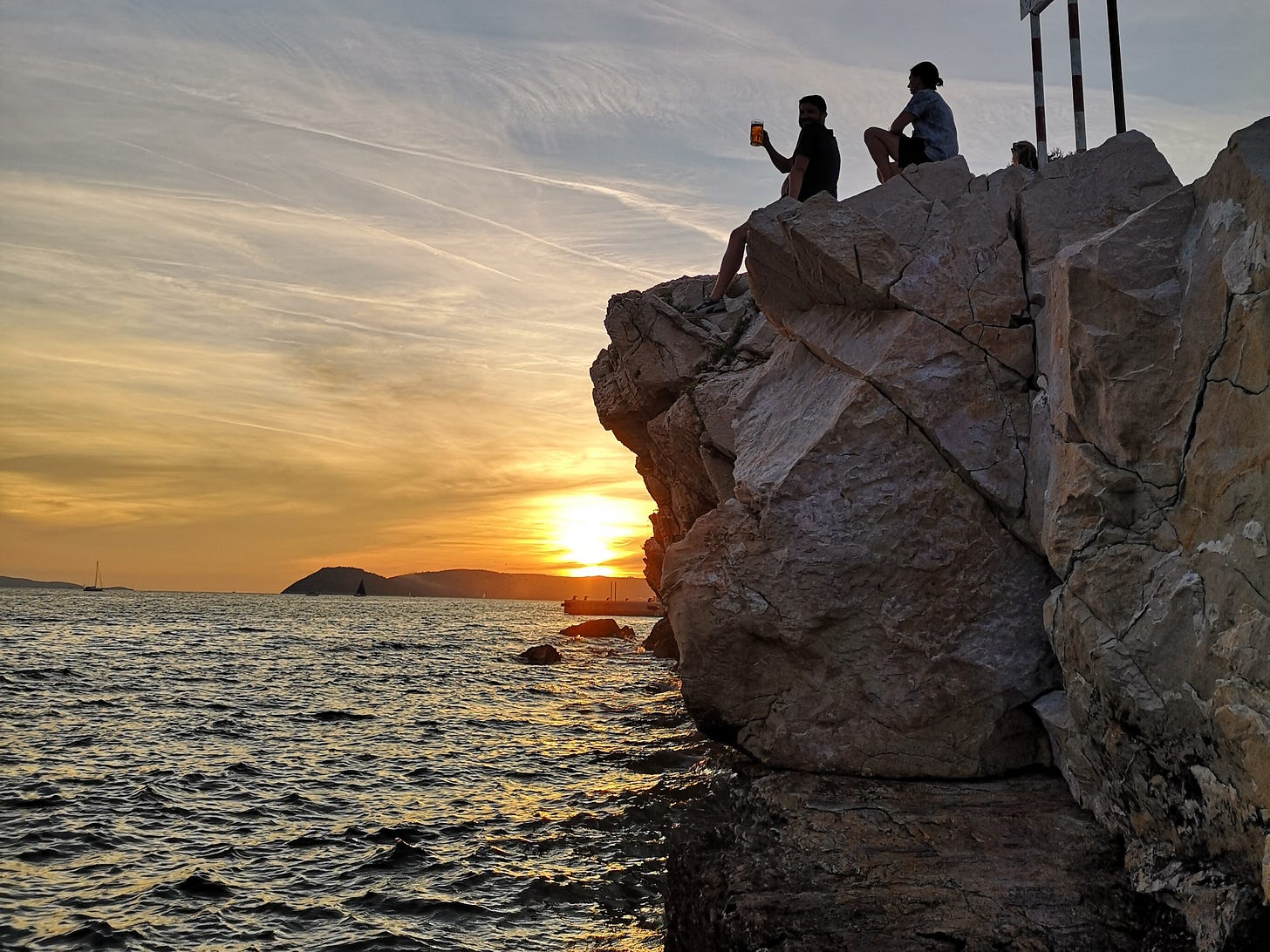 People sitting on a rock by the sea looking towards the sunset