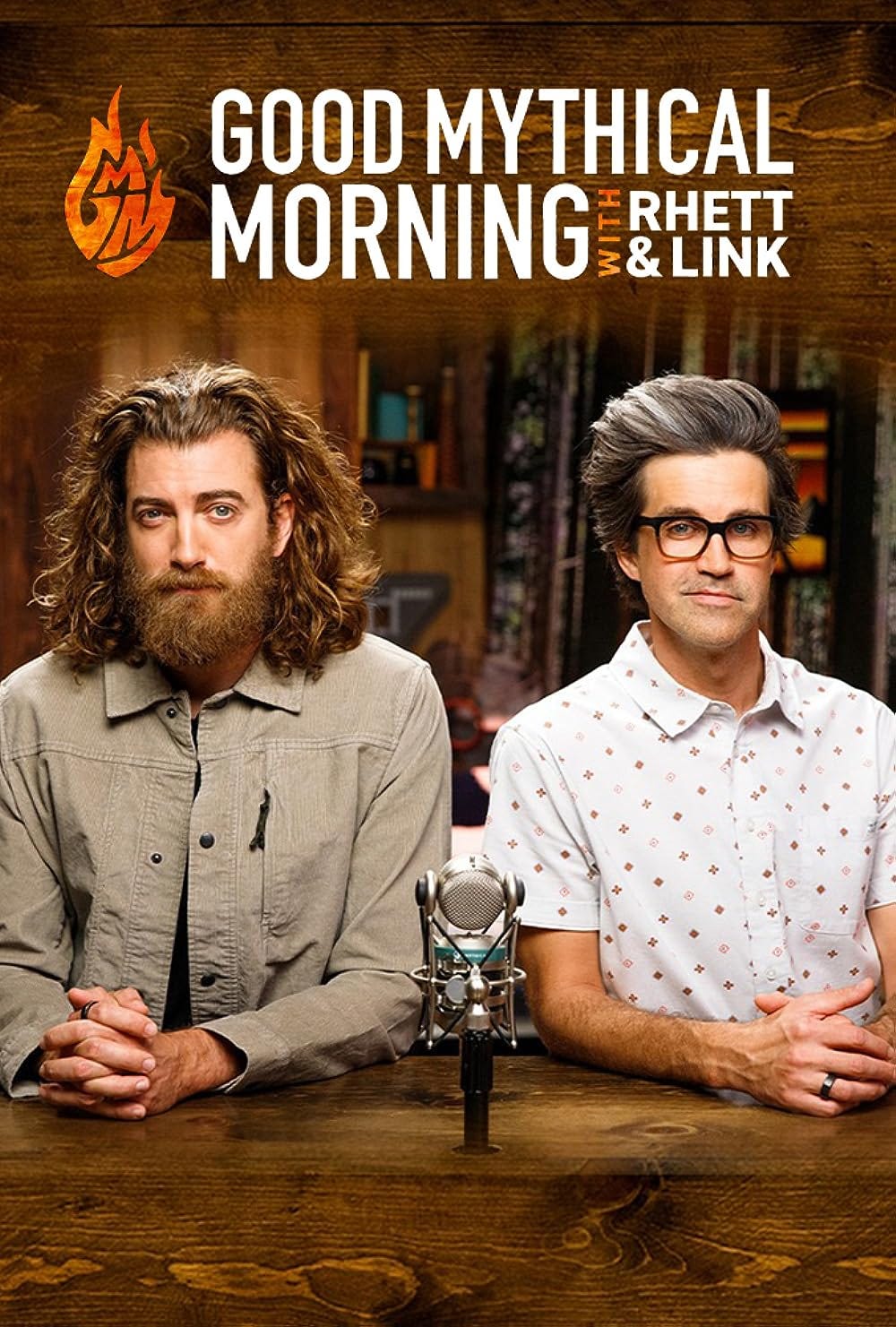 the logo for the youtube show good mythical morning with rhett and link. two white guys in their forties are staring at the camera. one has curly long brown hair and a beard, the other has graying black hair and glasses. they are sitting at a desk. 