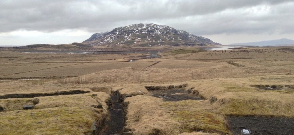 Big open greenish range, with excavation marks and a mountain behind