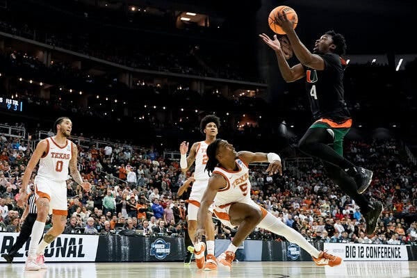 Miami guard Bensley Joseph, in a No. 4 jersey, flies in the air to shoot over three Texas players.