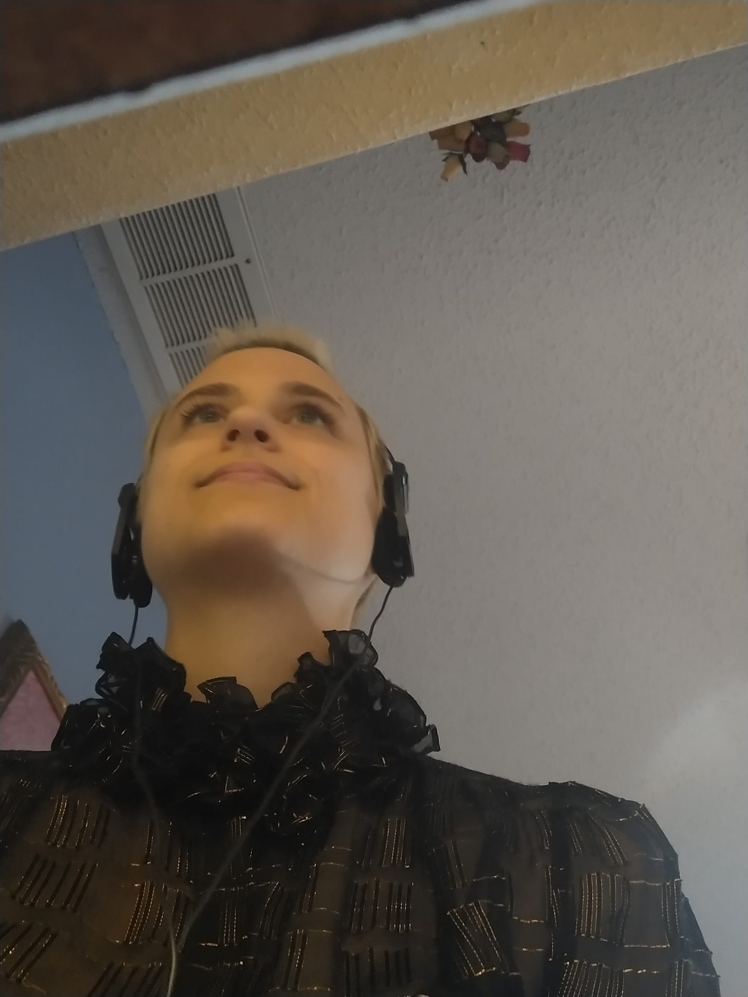 Jenna in a video call wearing headphones and a very frilly black and gold shirt.