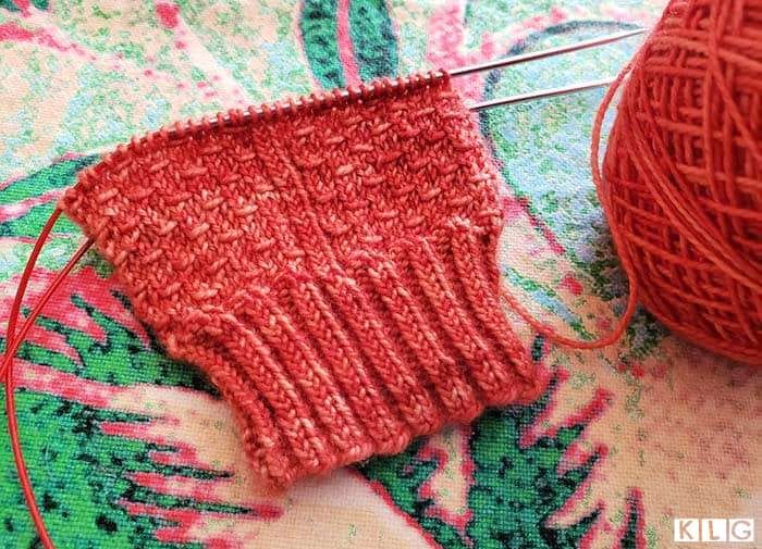 Knit through the back loop ribbed cuff with beginning of the dragon scale stitch pattern. Yarn Trader Studio Skinny Sock Yarn in Coral colorway.