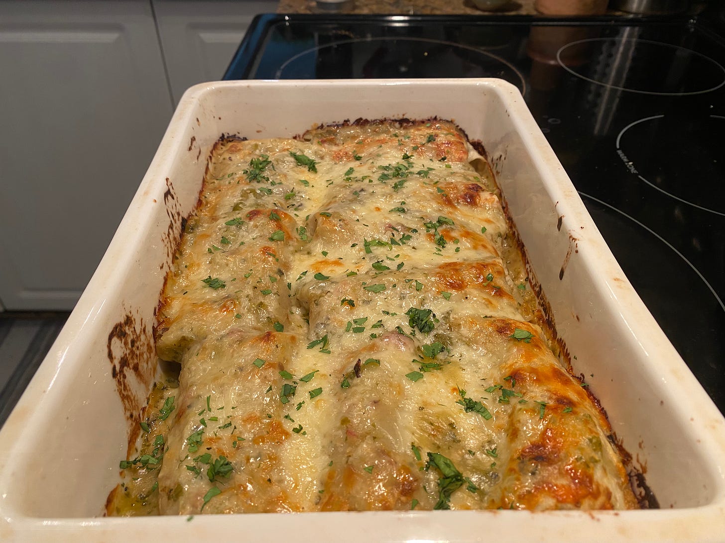 A white rectangular baking dish of enchiladas with melted browned cheese on top, sprinkled with cilantro.