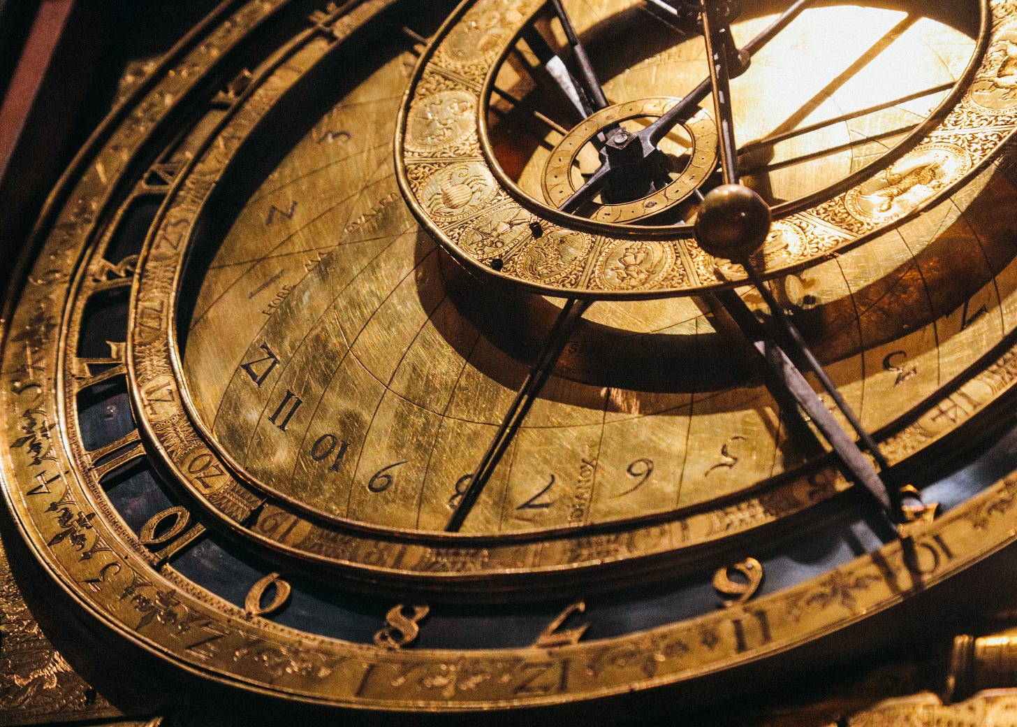 A close-up photo of a complex brass clock face, including several offset rings showing time, zodiac, etc.