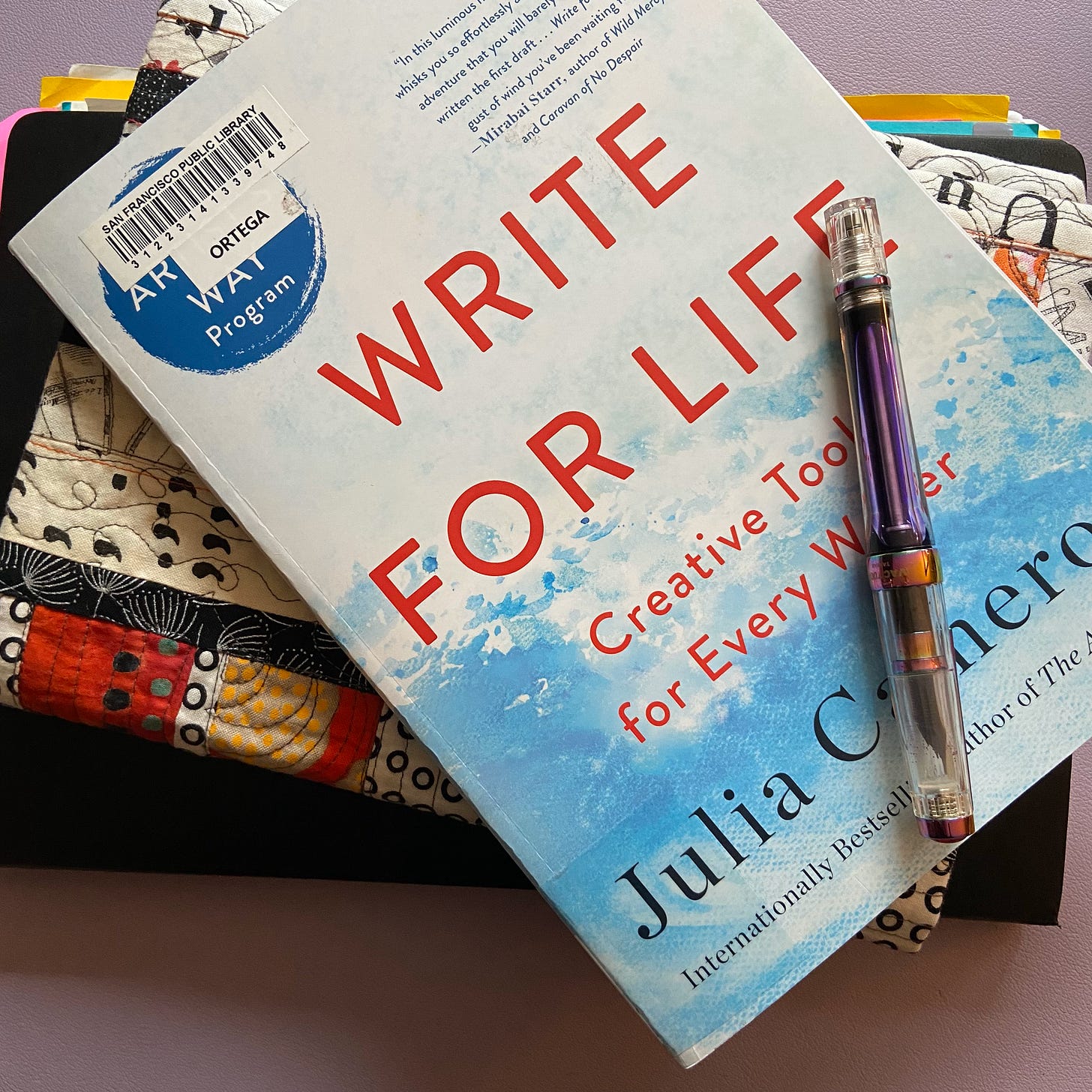 Stack of books showing a journal, a quilted journal cover, and Julia Cameron's Write for Life