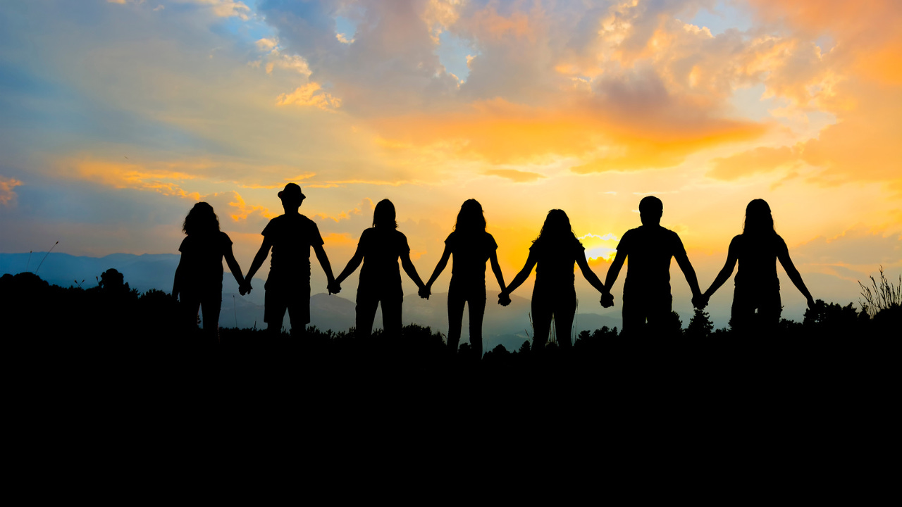A group of people holding hands in front of the sunset.