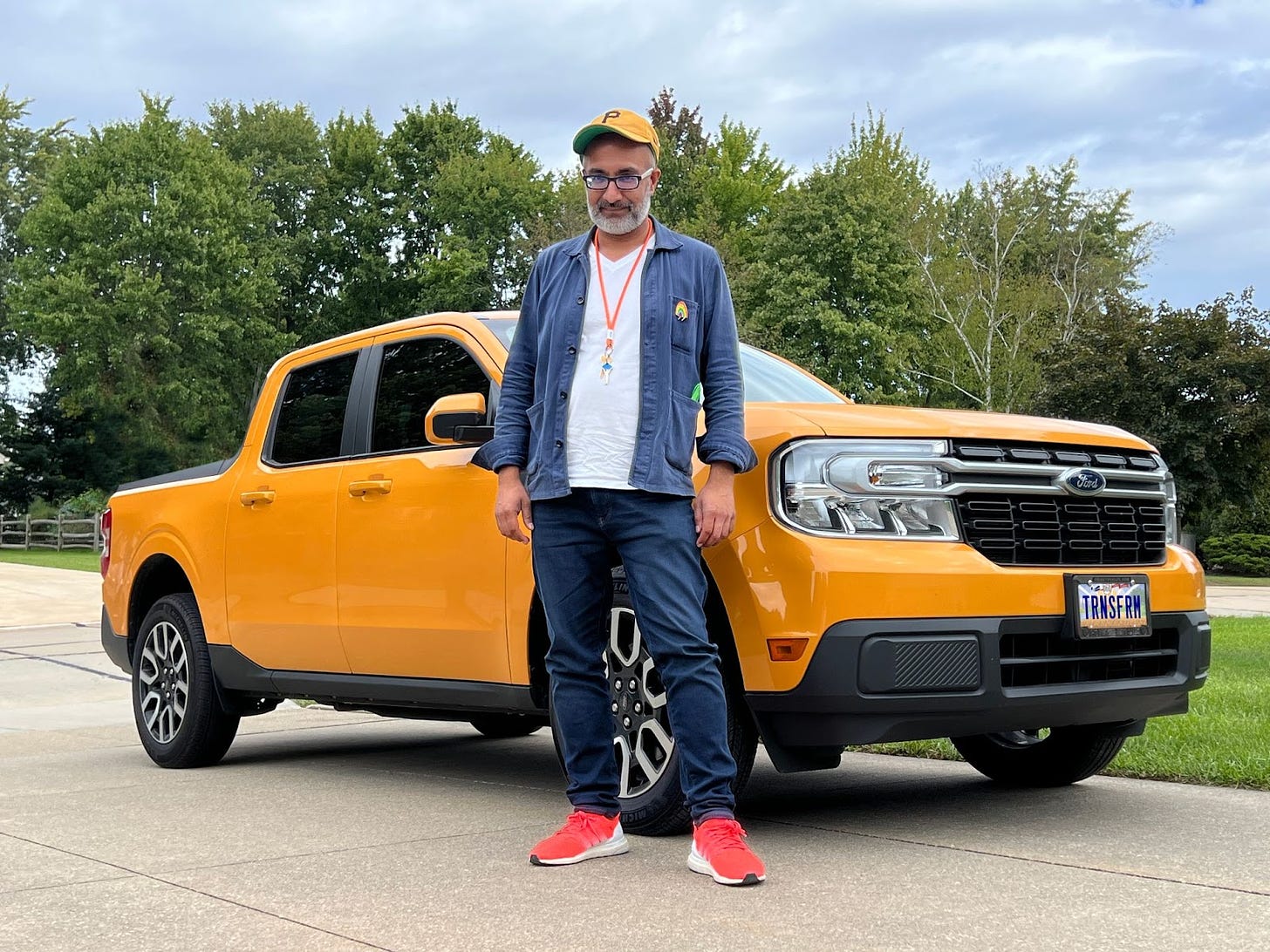 Bearded man with yellow "P" hat stands in front of a yellow hybrid pickup truck with the license plate, "TRNSFRM"