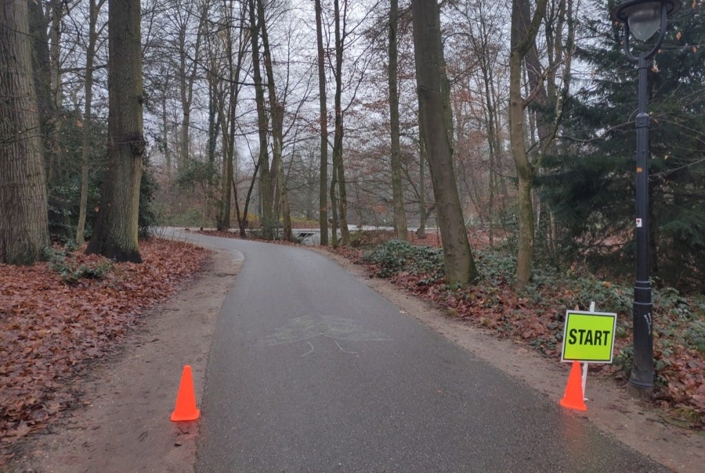 Start line marked by sign and two cones, either side of a path which is itself bordered by leaves and trees. A Christmas tree is chalked onto the path.