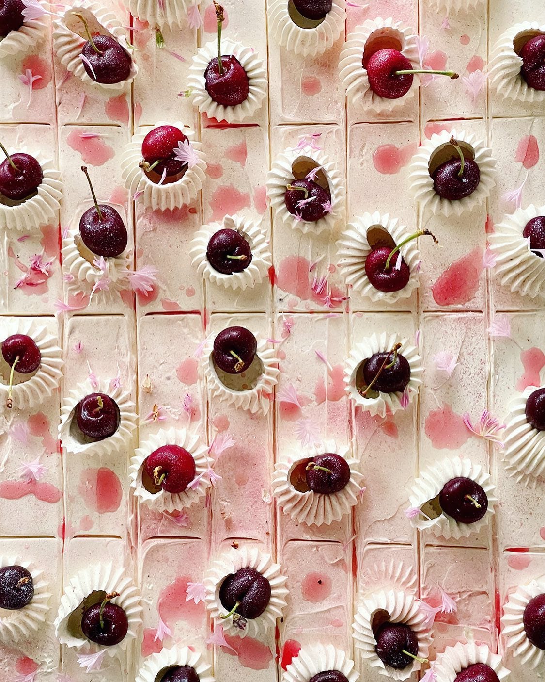 top-down view of a sheet cake decorated with cherries and pink flower petals