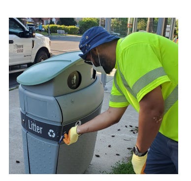 A photo of a city worker in a high-viz vest inspecting an on-street litter bin