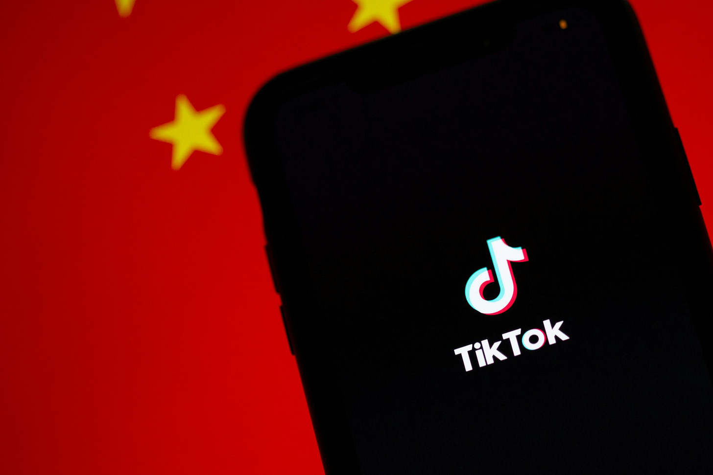 Imagem em cores de celular com o aplicativo TikTok diante de bandeira da China.