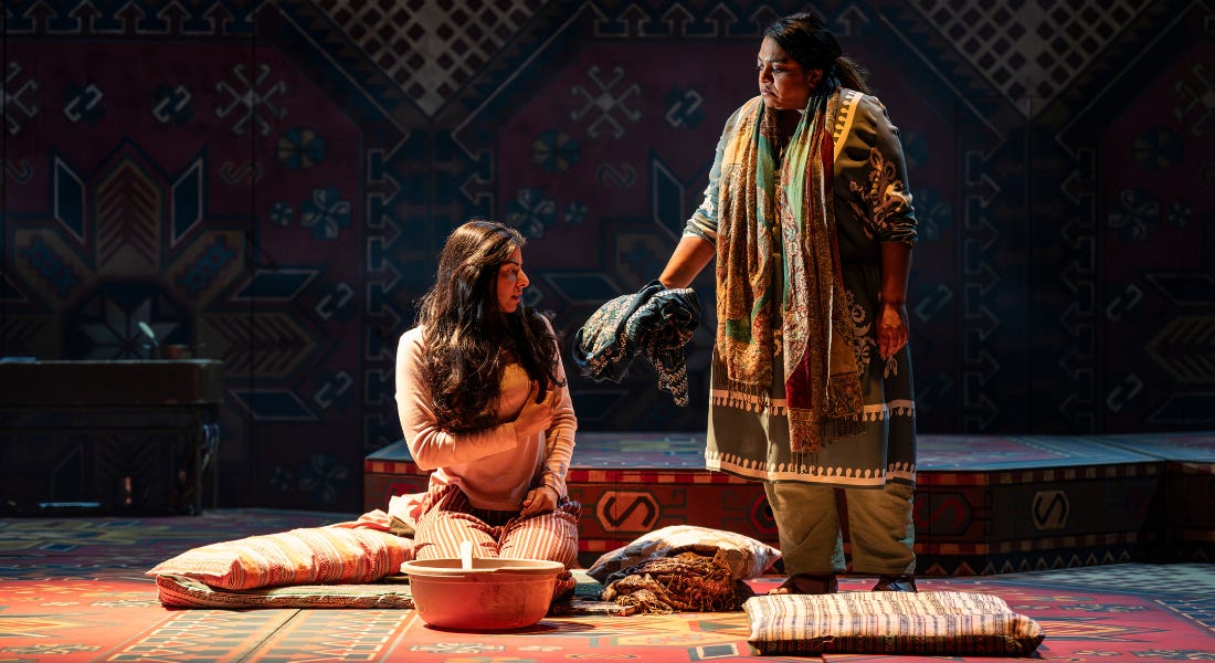 Two women wearing colourful Indian clothing on a stage, standing on tapestry and with tapestry behind them Two women wearing colourful Indian clothing on a stage, standing on tapestry and with tapestry behind them