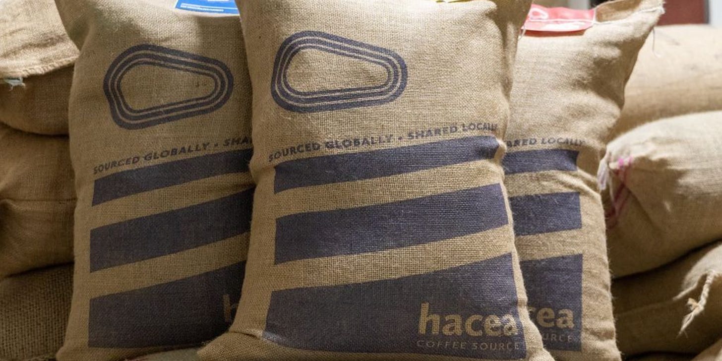 Close up of burlap sacks filled with green coffee featuring the Hacea Coffee logo