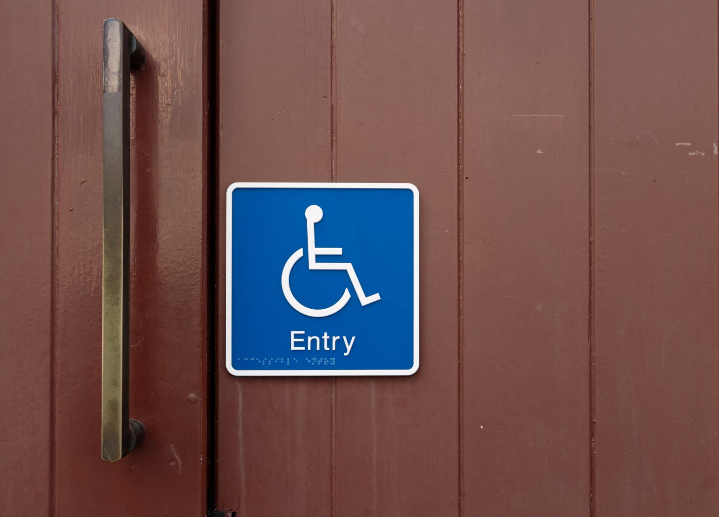 Wheelchair symbol sign reading "Entry" mounted on a door.