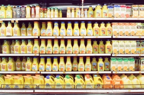 grocery shelves with orange juice bottles and cartons lined up