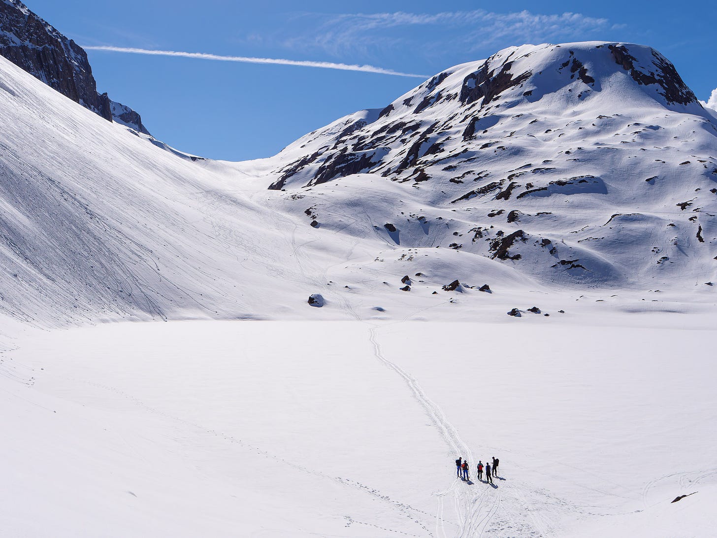 A group of ski tourers pausing to regroup while crossing a frozen mountain lake.