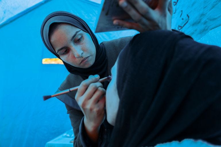 Noor applying makeup to Aya's face in the blue light of the tent.